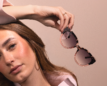 Woman holding a pair of sunglasses with a neutral background